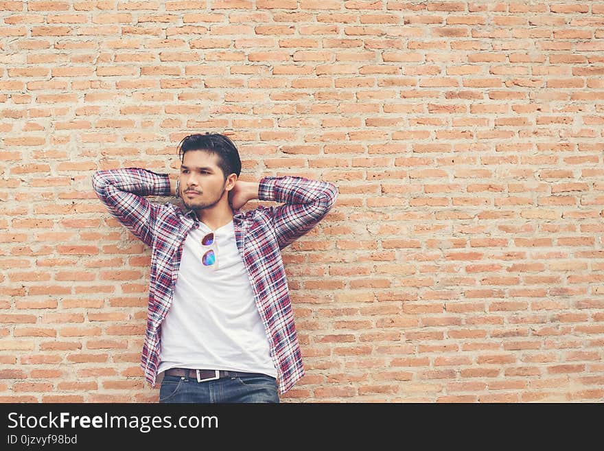 Young handsome hipster man wearing plaid shirt and jeans against a brick wall.