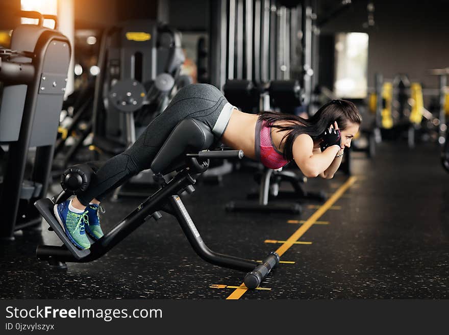 Athletic young woman doing hyperextension in the gym. Woman flexing back and abdominal muscles on bench.