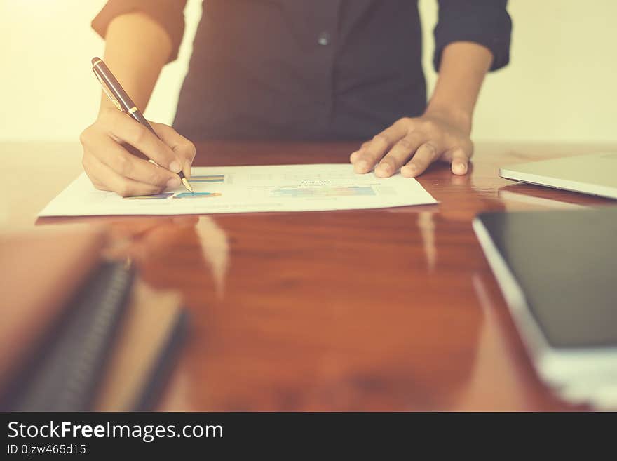 Woman`s hand with a pen writing on the business paper. Report chart,busy at work.