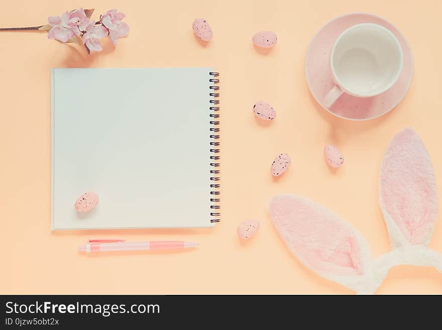 Easter holiday background with notebook and pen, cup for coffee, bunny ears and easter eggs. Copy space background. Flat lay. Toned