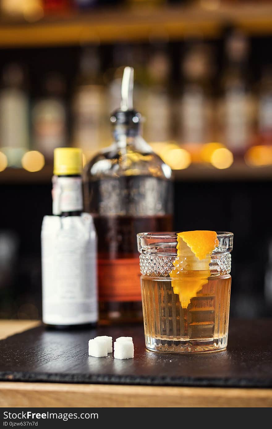 Glass of whiskey cognac or brandy with lemon and ice cubes standing on the bar counter with a bottle on the background