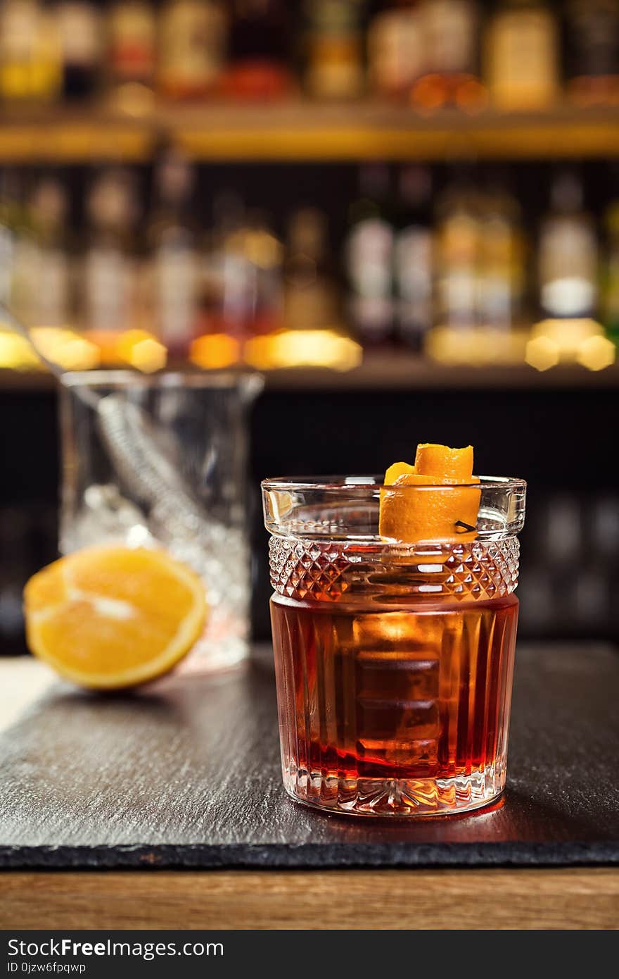 Glass of whiskey cognac or brandy with lemon and ice cubes standing on the bar counter with a bottle on the background