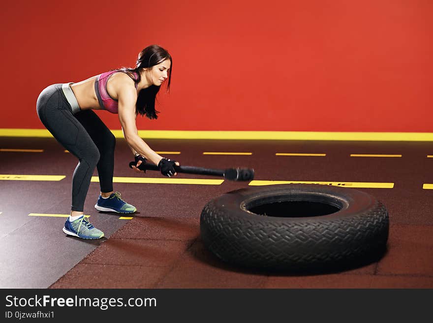 Fit young woman workout in the gym with hammer and tractor wheel.