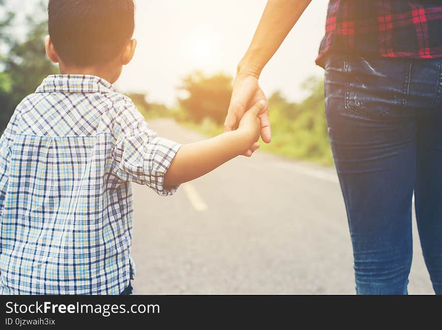 Mother holding a hand of his son in summer day walking on the street.