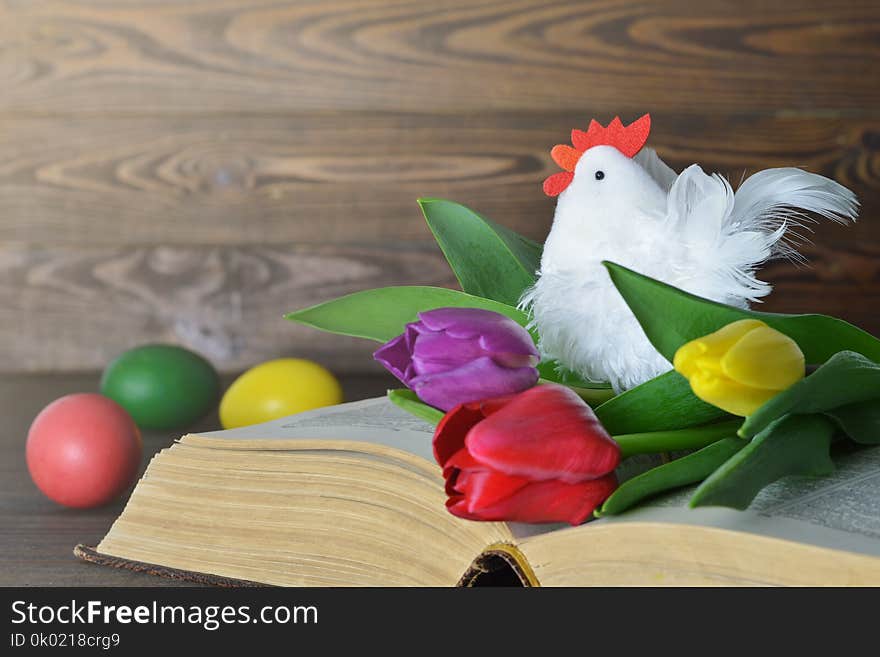 Easter card with colored Easter eggs, rooster toy and tulips on the book