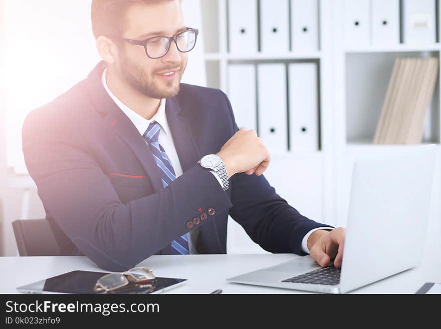 Businessman using laptop computer while sitting at the desk in office. Focus at cheerful smiling bearded man wearing