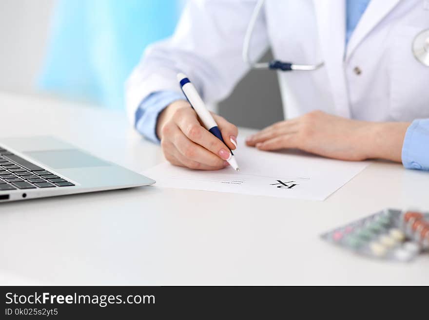 Female doctor filling up prescription form while sitting at the desk in hospital closeup. Physician finishing u