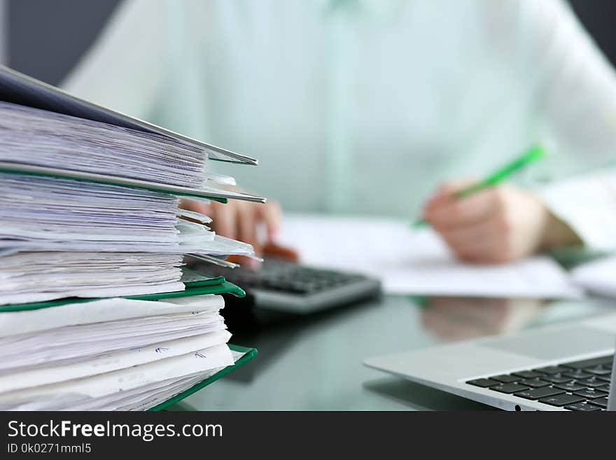 Bookkeeper or financial inspector making report, calculating or checking balance. Binders with papers closeup. Audit and tax service concept. Green colored image background.