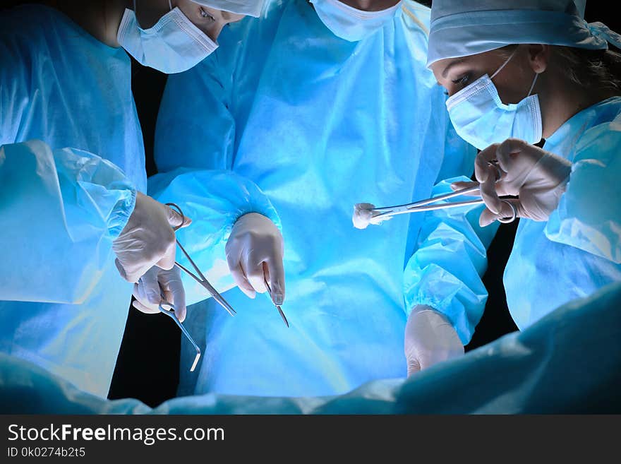 Group Of Surgeons At Work In Operating Theater Toned In Blue