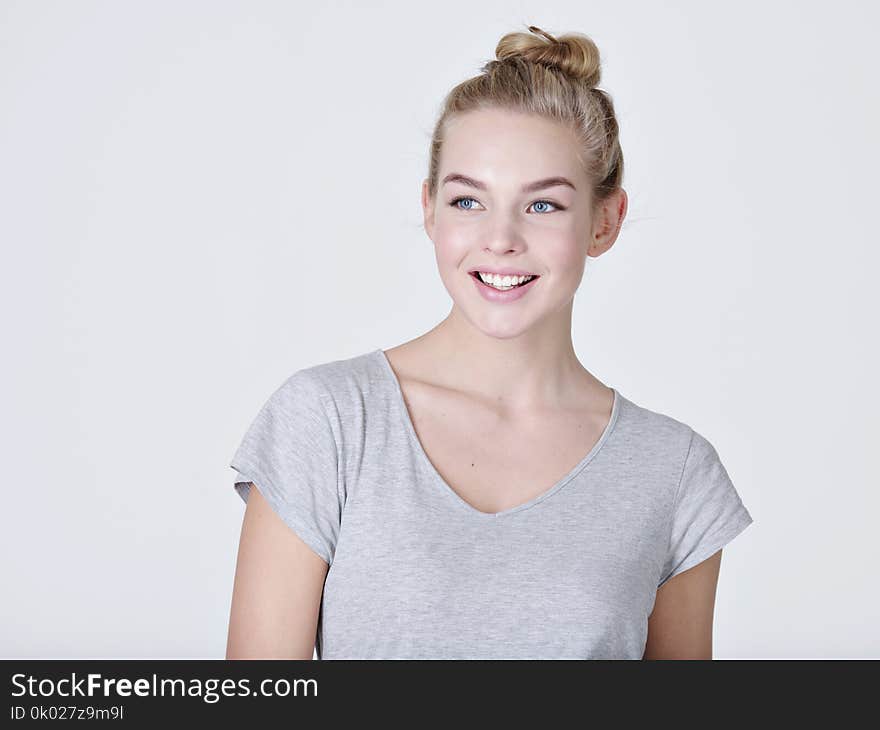 Portrait of a beautiful young smiling girl. Female face with toothy smile. Attractive blond girl poses at studio in a casual grey t shirt. Portrait of a beautiful young smiling girl. Female face with toothy smile. Attractive blond girl poses at studio in a casual grey t shirt