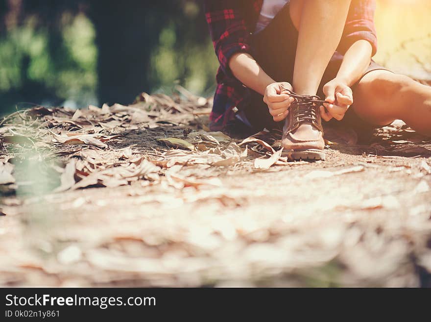 Young woman hiker stops to tie her shoe on a summer hiking trail