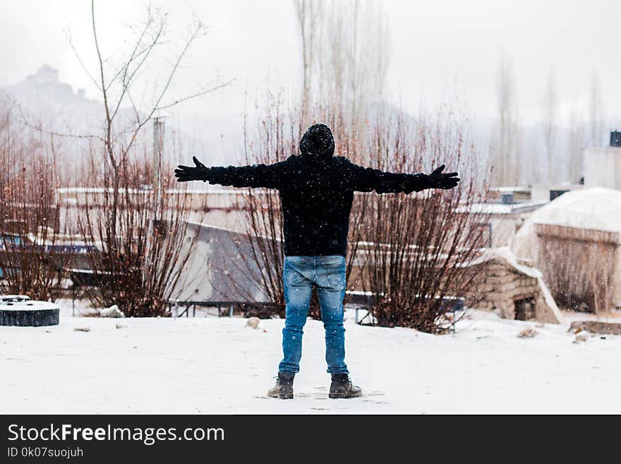 Person Wears Black Jacket and Blue Denim Jeans Standing on Snow Covered Field