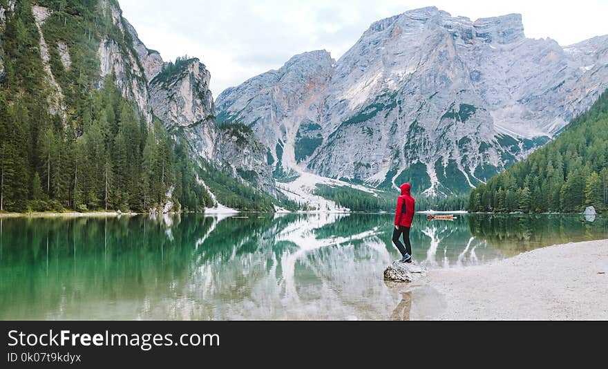 Man Wearing Red Hoodie Standing Near Body of Water With View of Mountains