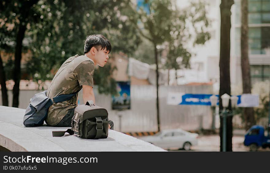 Man in Green and Beige Camouflage T-shirt Siting Beside Bag at Daytime