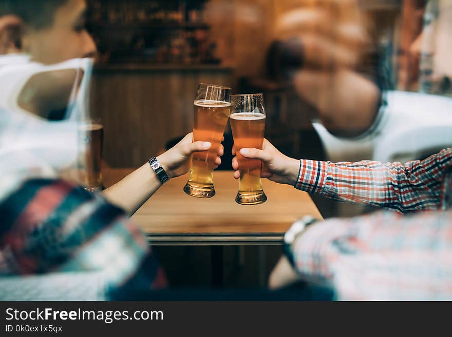 Close up hands of friends sitting at the pub cheers with beers glasses trough window.