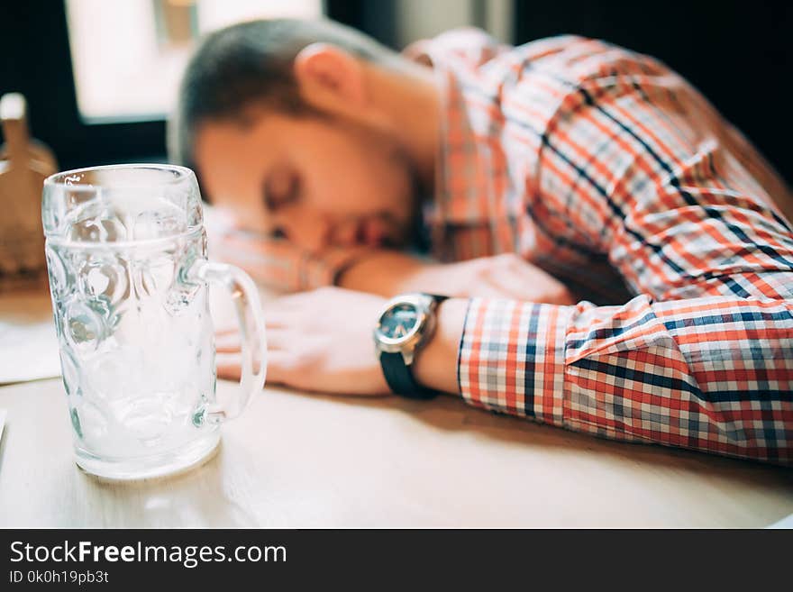 Drunk again. Drunk male customer leaning at the bar counter and sleeping while glass with beer standing near him