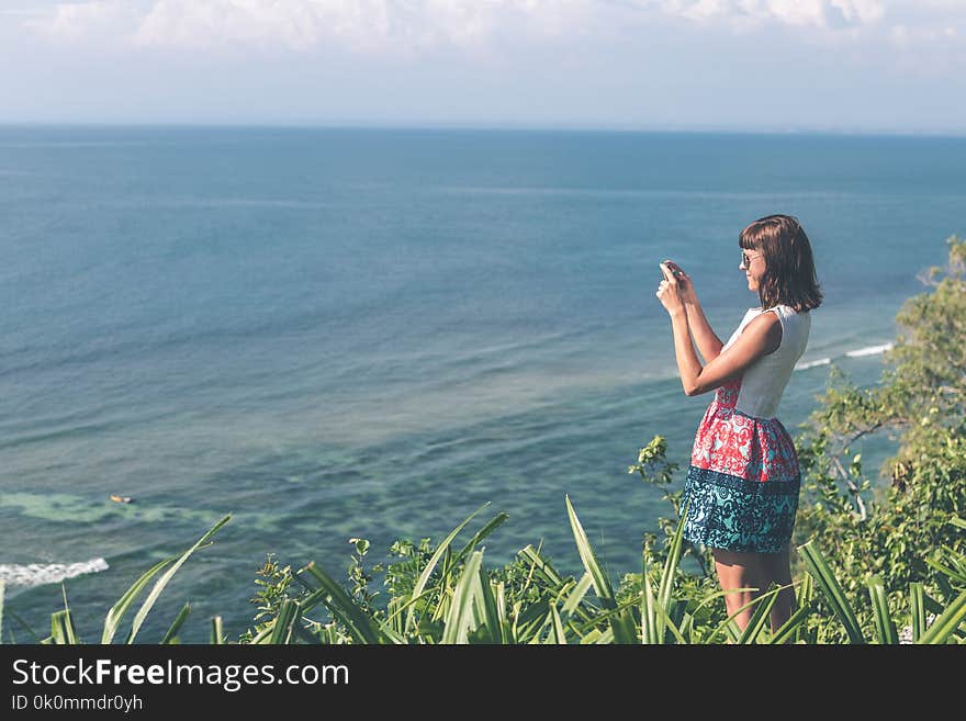 Woman Standing White and Blue Floral Dress Holding Smartphone in Grass Area