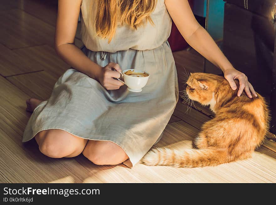 Young woman is drinking coffee and stroking the cat