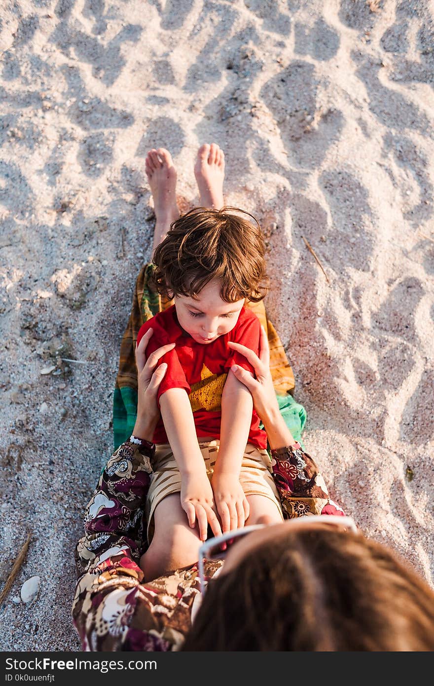 Child with mom on the beach. The boy is playing with his mother. The kid lies on the sand. A women is resting with her son at the seaside.