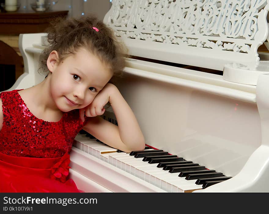 A nice little girl is playing on a big white piano. The concept of musical and aesthetic education of a child. A nice little girl is playing on a big white piano. The concept of musical and aesthetic education of a child.