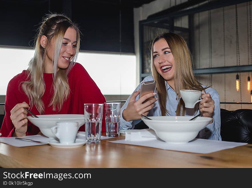 Female Friends Having Lunch Together At The Restaurant. Two young women using a mobile phone during lunch