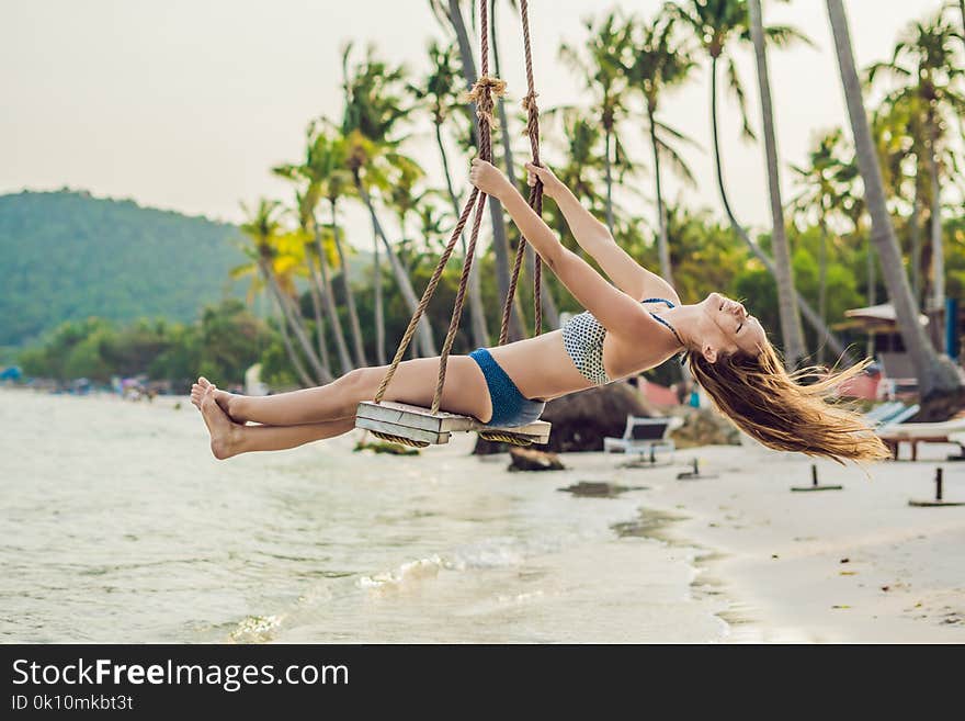 Vacation concept. Happy young woman sitting on swing enjoying sea view.