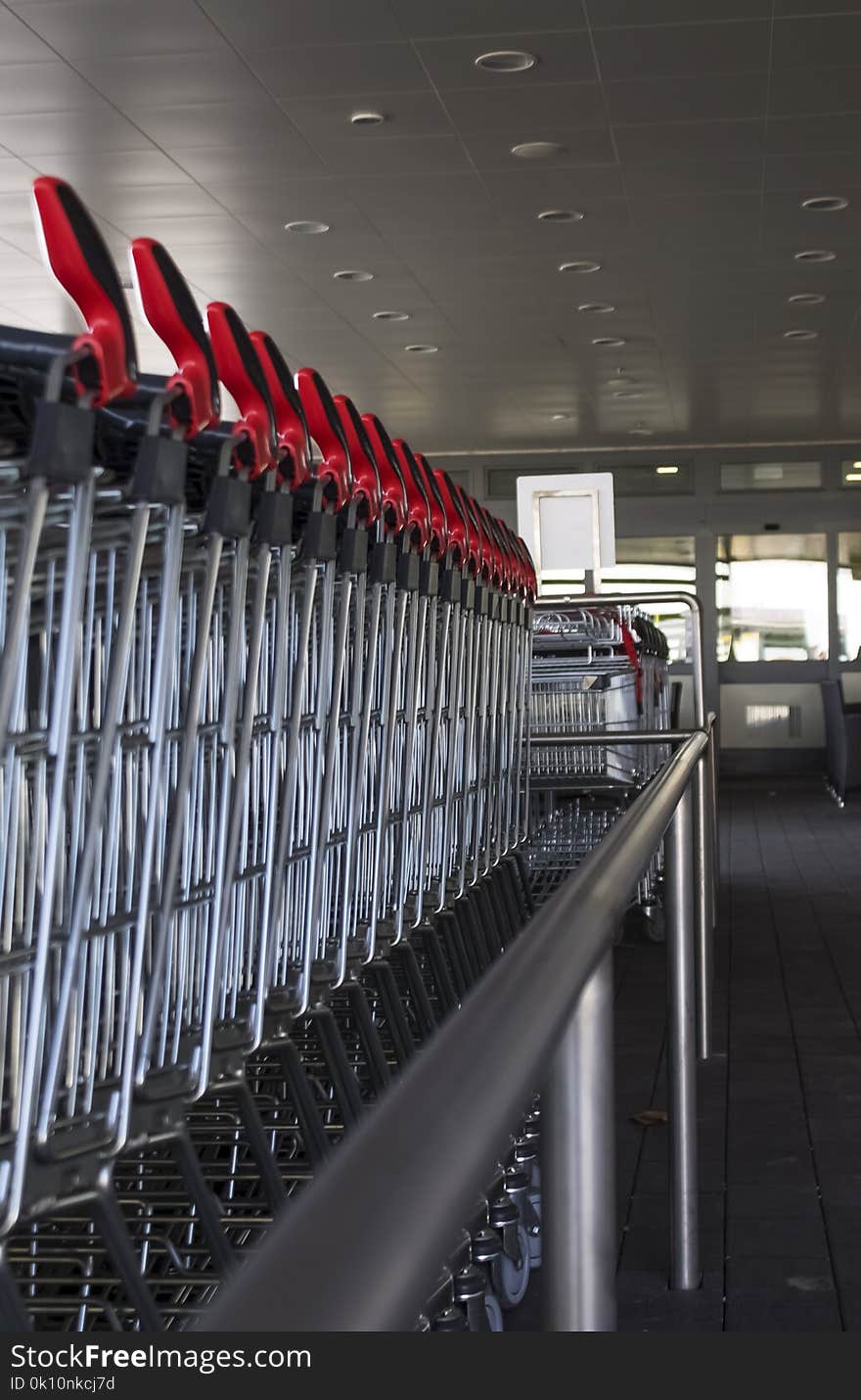 Many shopping carts in a row with red handle in front of supermarket