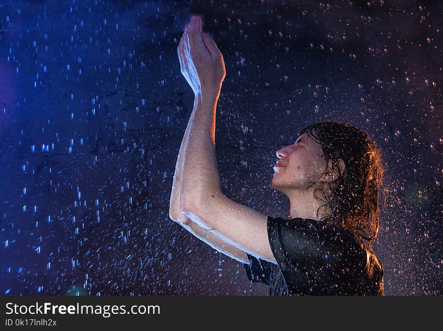 Attractive young man in black wet clothes under the rain and splash of water, studio photo