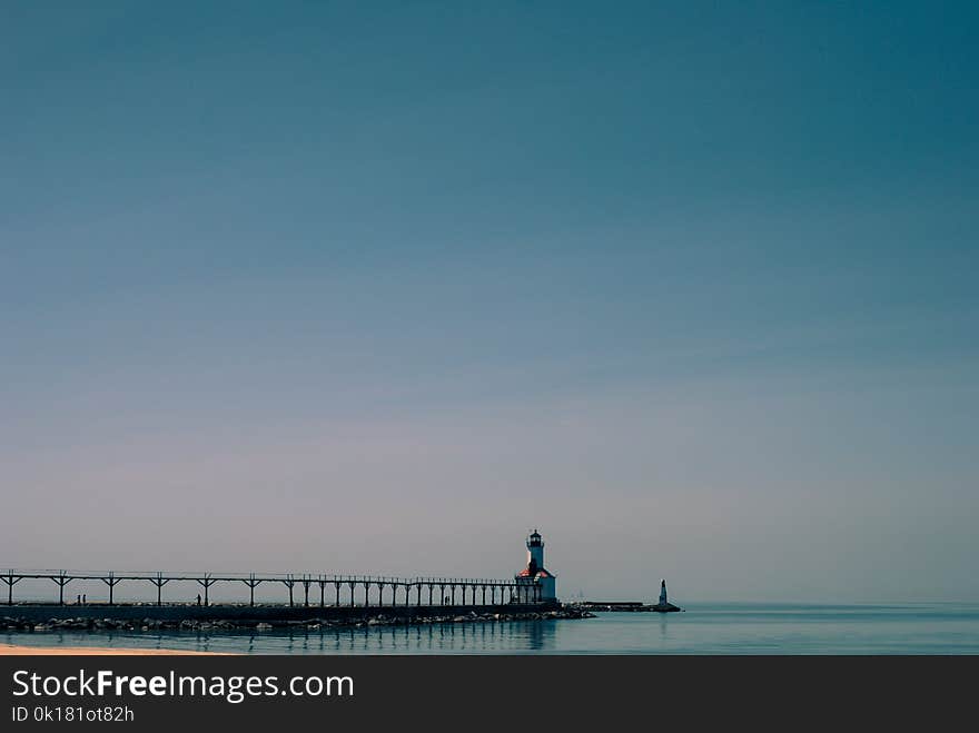 Dock Near White and Brown Concrete Lighthouse Surrounded by Calm Body of Water