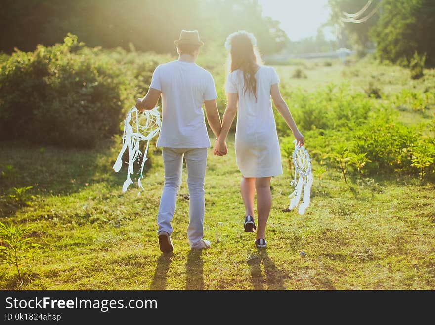 Coupe With White Dress and Suit Holding a White Dreamcatcher While Walking on Green Grass