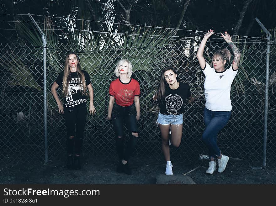 Four Women Leaning on Gray Steel Fence