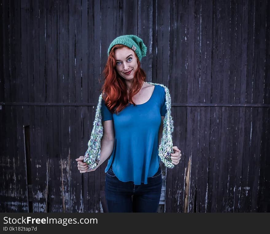 Woman in Blue Scoop-neck Shirt and Green Beanie Cap Standing in Front of Black Wooden Fence