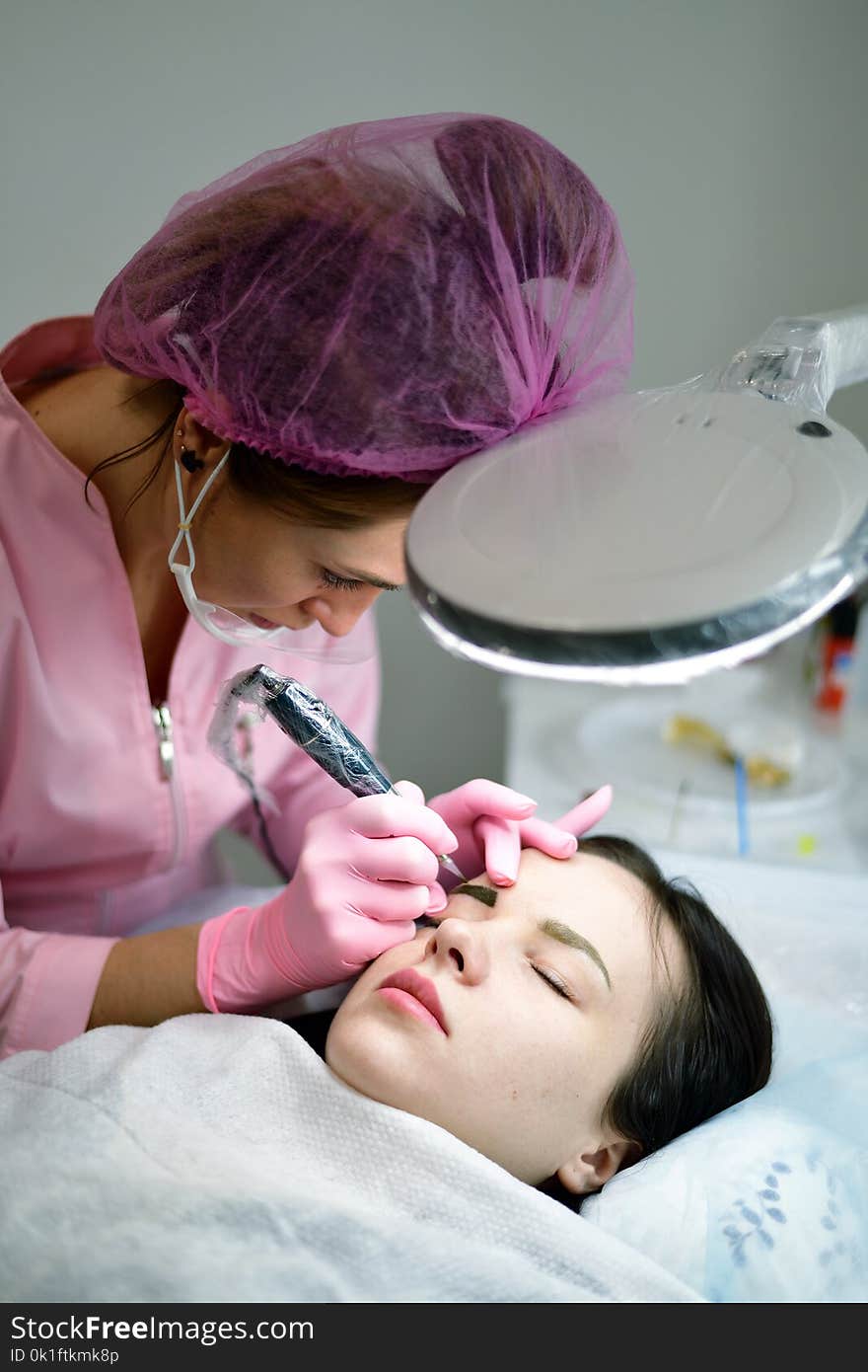 the master does the tattoo on the eyebrows to the girl. the master does the tattoo on the eyebrows to the girl.