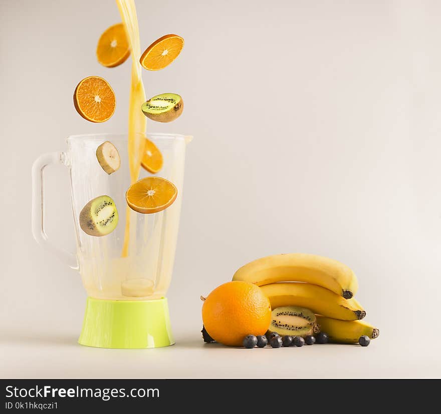 Flying ingredients making smoothies from oranges, kiwi and bananas, vegetarian healthy food, fruit lined around a green blender, space for text