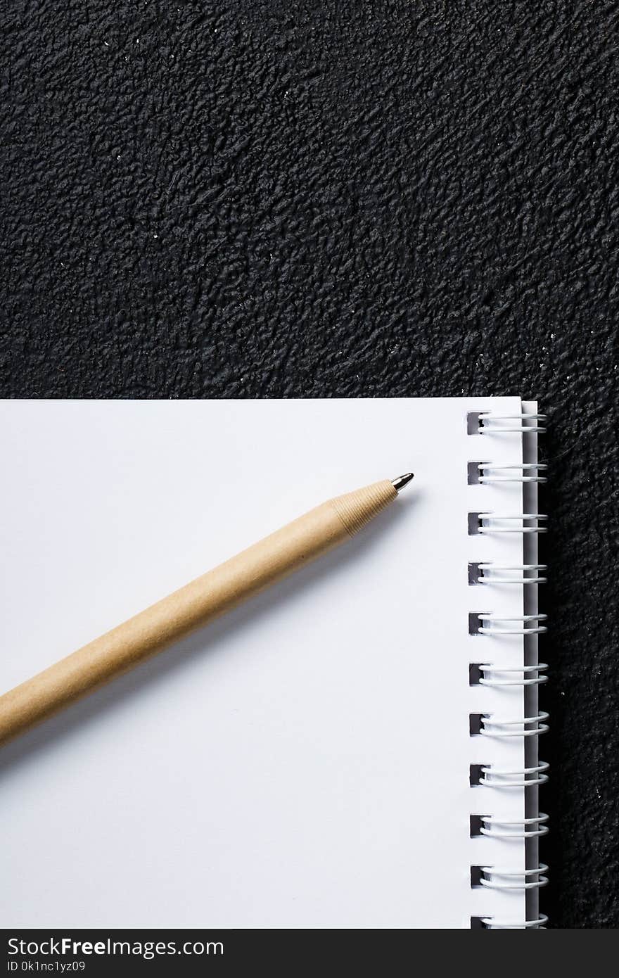 Top view of closed black cover notebook with pencil on black desk background. Top view of closed black cover notebook with pencil on black desk background