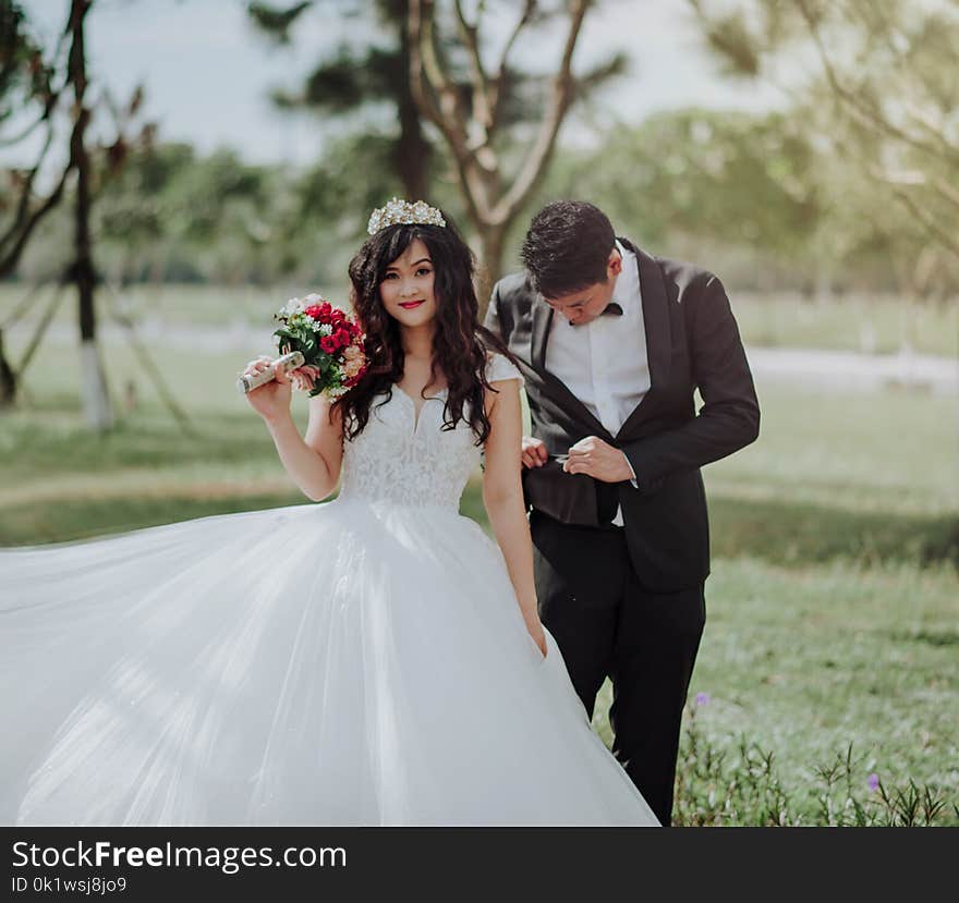 Woman in Wedding Dress Holding Flower With Man in Black Blazer