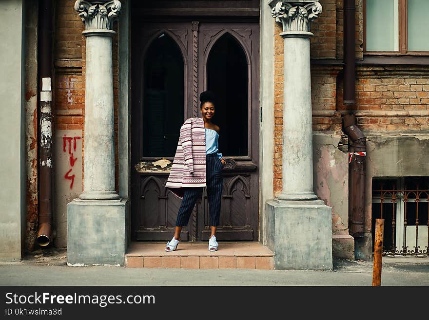 Woman in Blue Strapless Top and Black Pants Standing Next to Brown Wooden Door