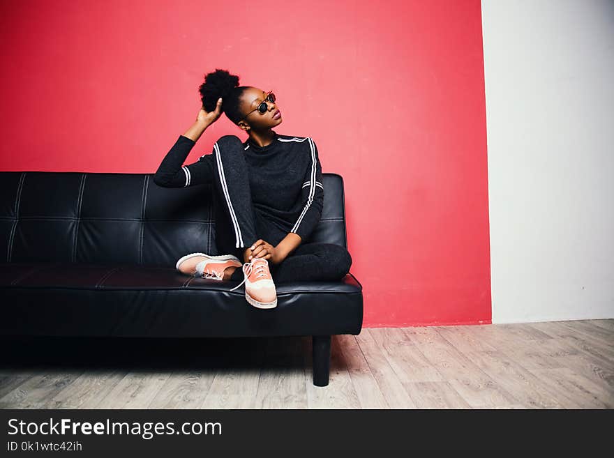 Woman With Black-and-white Sweater With Pants Sitting on Black Leather Sofa Beside Red Painted Wall