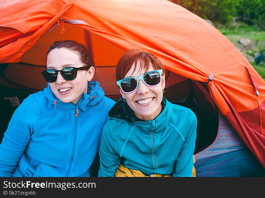 Two girls are sitting in a tent. Girlfriends communicate in nature. Women in sleeping bags. Friends in the campsite. Smiling brunettes talking. Two girls are sitting in a tent. Girlfriends communicate in nature. Women in sleeping bags. Friends in the campsite. Smiling brunettes talking.