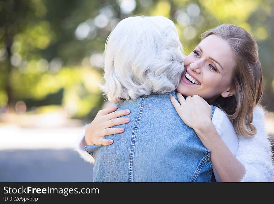 Love you forever. Happy young sincere women walking in the square while expressing love and hugging aged mother. Love you forever. Happy young sincere women walking in the square while expressing love and hugging aged mother