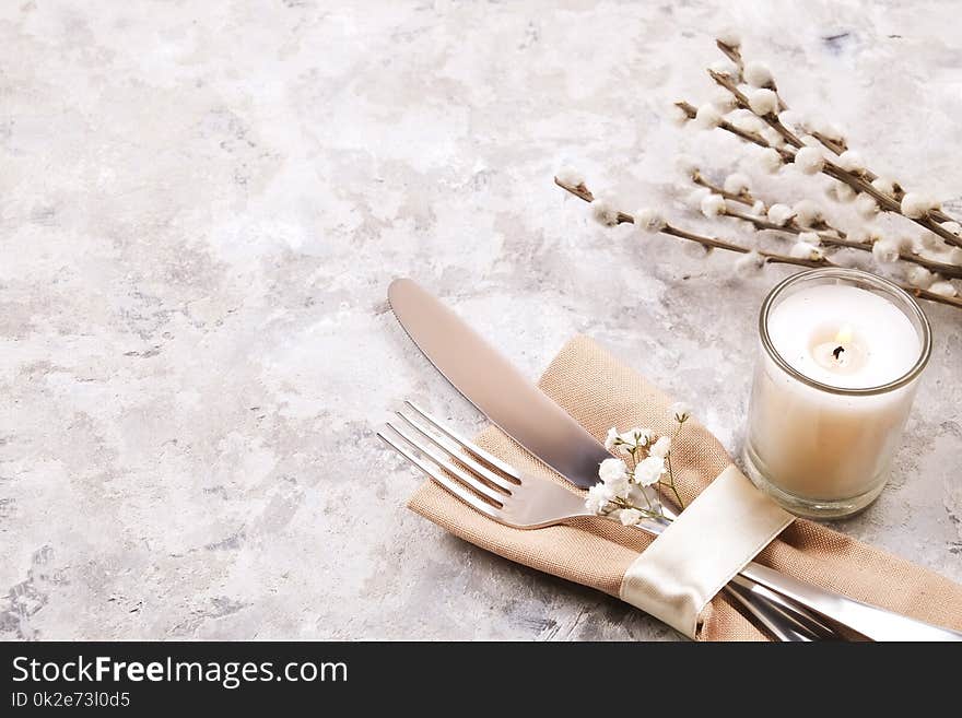 Easter table setting composition: fork, knife candle, wildflowers, willow on plate w/ napkin, white stucco plaster texture background. Close up, top view, copy space. Easter table setting composition: fork, knife candle, wildflowers, willow on plate w/ napkin, white stucco plaster texture background. Close up, top view, copy space