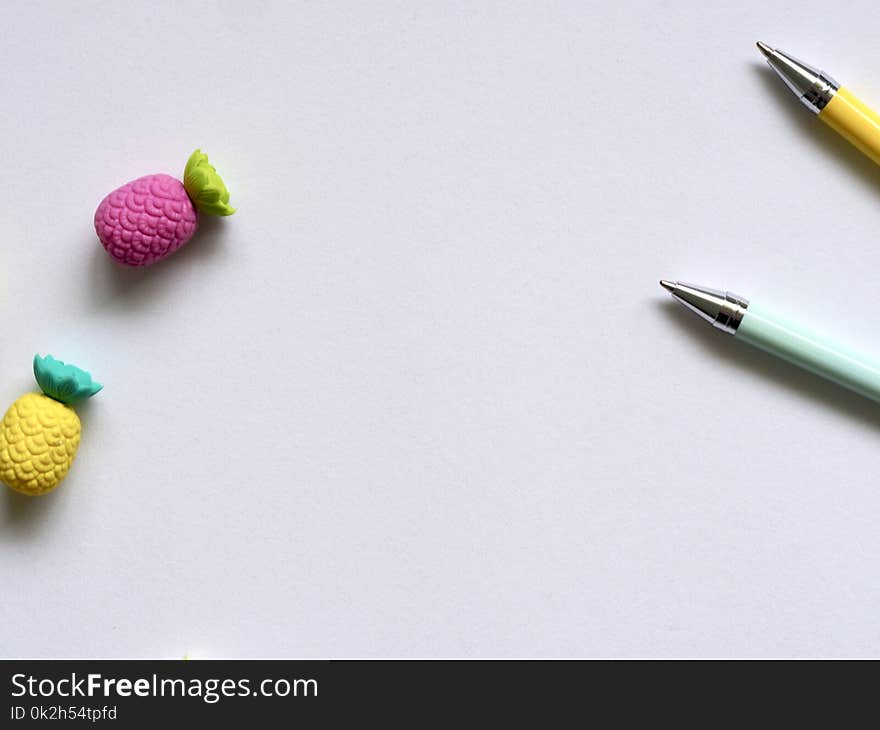 Photo of Two Purple and Yellow Pineapple Erasers Near Pens