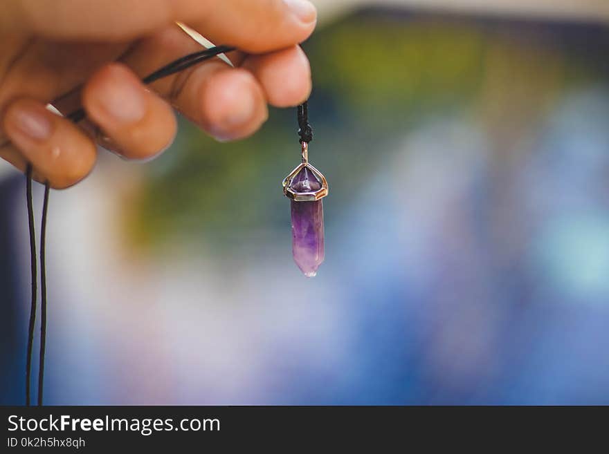 Person Holding Black Necklace With Purple Stone Pendant