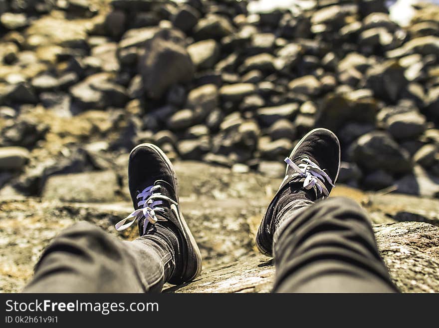 Shallow Focus Photography of Person Wearing Gray Jeans Sitting in Front Rocks