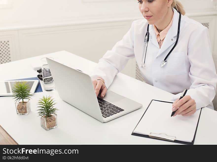 Doctor Using Laptop And Writing Notes At Office