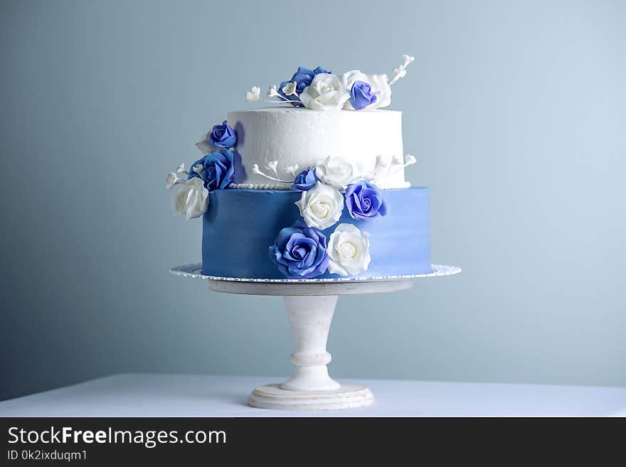 Beautiful two tiered white and blue wedding cake decorated with flowers sugar roses on the table. The concept of elegant holiday desserts