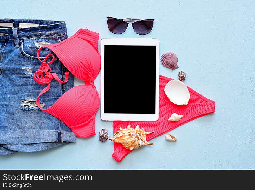Female summer bikini swimsuit and accessories on blue with tablet and sunglasses. flat lay, top view