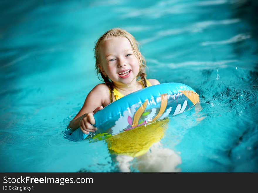 Cute little girl playing with inflatable ring in indoor pool. Child learning to swim. Kid having fun with water toys.