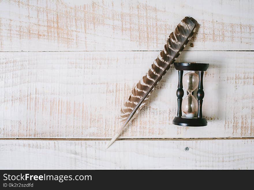 Hourglasses And Fether Lie On A Wooden Table. Top View. Layflat.