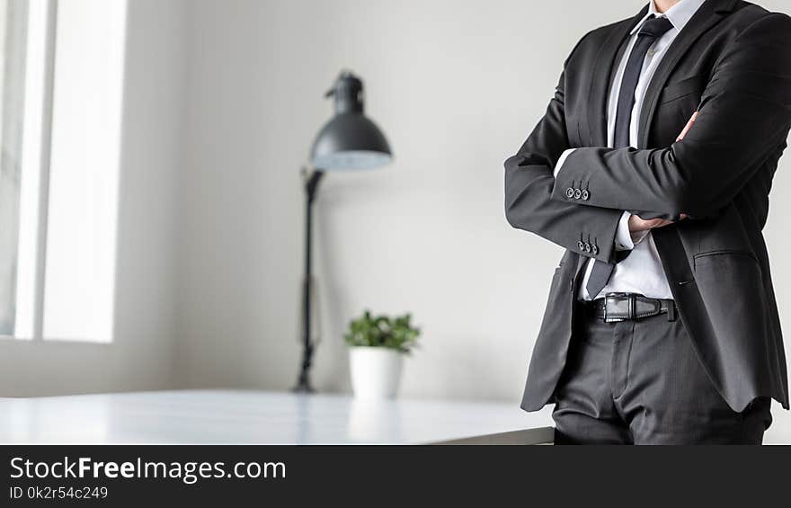 Businessman standing in office with crossed arms, close up view of his body.